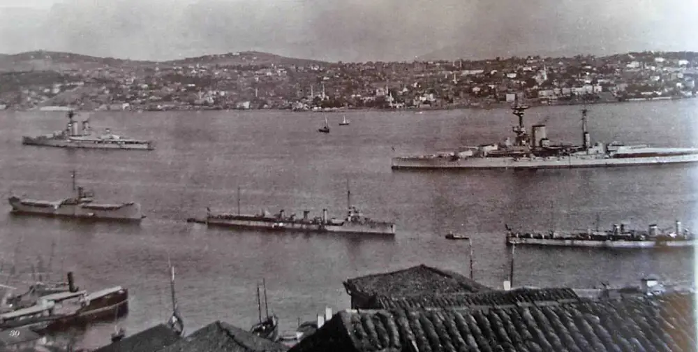 This vintage photograph provides a glimpse into Istanbul's maritime history. The grayscale image showcases a fleet of naval ships anchored in the Bosphorus Strait, juxtaposed against a backdrop of the city's undulating hills and buildings. The traditional tiled rooftops in the foreground serve as a testament to the city's rich architectural heritage. The presence of both military and civilian vessels highlights Istanbul's strategic importance and its role as a bustling port city during this era. The image evokes nostalgia, transporting viewers back to a bygone epoch when sea vessels were the pride of nations and symbols of power.