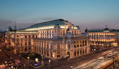 Evening view of Vienna State Opera with illuminated facade, bustling traffic, and historic cityscape backdrop