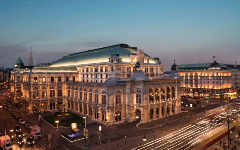 Evening view of Vienna State Opera with illuminated facade, bustling traffic, and historic cityscape backdrop